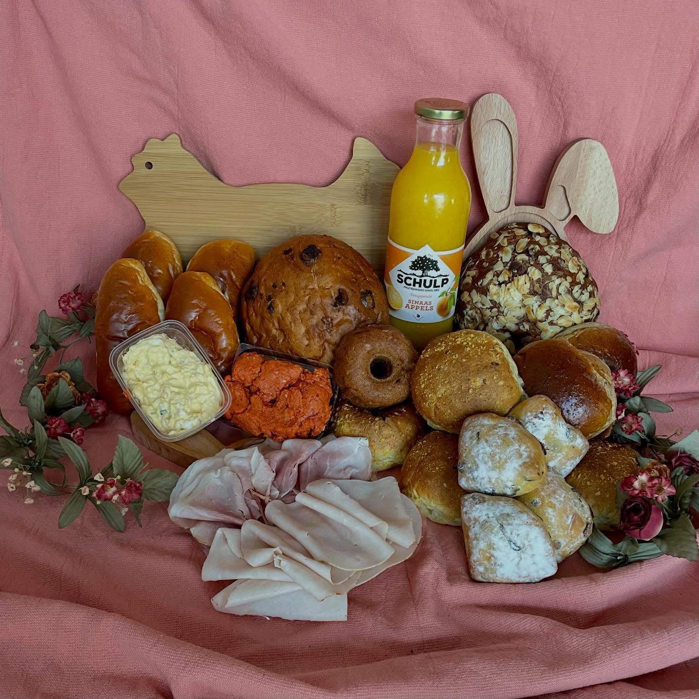 Ontbijt van de bakker: zachte broodjes, krentenbrood, een notenbrood en een fles sinaasappelsap